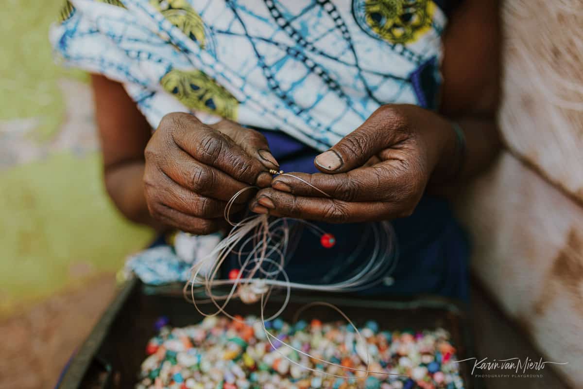 prime vs zoom lens | Copyright Karin van Mierlo for Photography Playground. Photo: A woman strings beads for a necklace, Acholi Quarter, Kampala Uganda