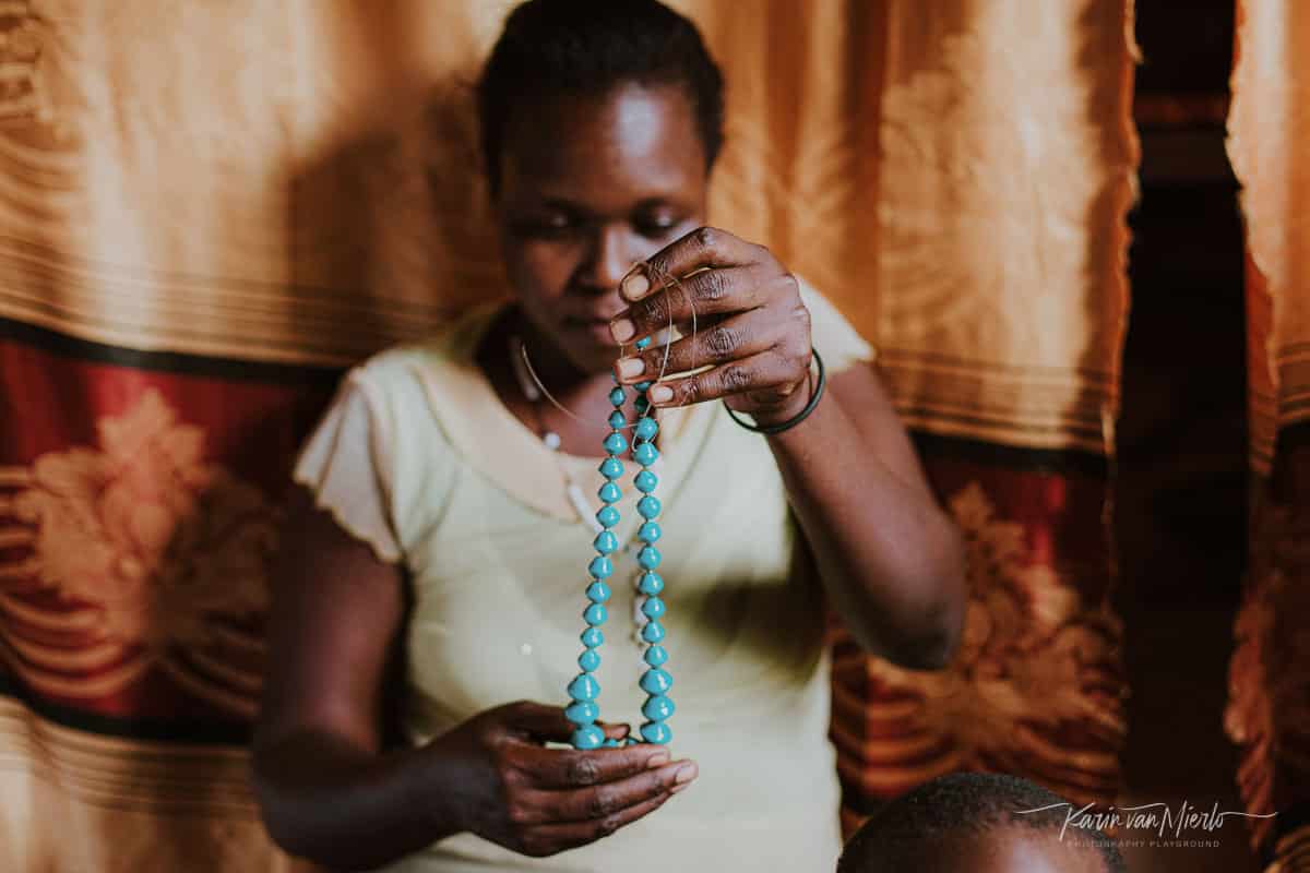 prime vs zoom lens | Copyright Karin van Mierlo for Photography Playground. Photo: A woman looks at a necklace she just made, Acholi Quarter, Kampala Uganda